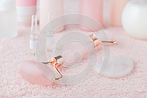 Beautiful composition of spa and wellness products, facial rose quartz roller and face serum on pastel pink background