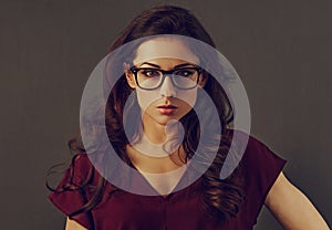 Beautiful concentrated serious brunette business woman looking in eye glasses with curly hair style in red silk blouse on grey