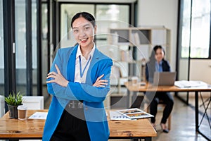 A beautiful and confident Asian businesswoman is standing with her arms crossed in a modern office