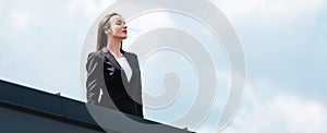 beautiful, confident businesswoman standing on rooftop, smiling and looking away.