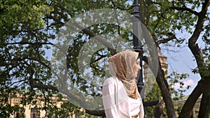 Beautiful confident muslim woman in hijab walking in park and covering her face from sun, sunny day outdoors