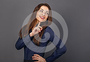Beautiful confident thinking toothy smiling business woman with finger under the face in blue shirt on grey background with empty