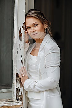 a beautiful, confident woman in a white suit at the old window. image of bride