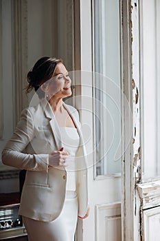 a beautiful, confident woman in a white suit at the old window. image of bride