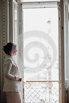 a beautiful, confident woman in a white suit at the old window. image of bride