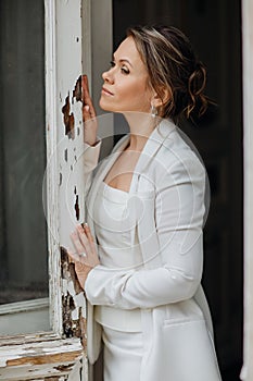 a beautiful, confident woman in a white suit at the old window. image of bride
