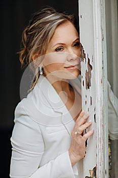 a beautiful, confident woman in a white suit at the old window. image of bride