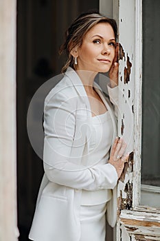 a beautiful, confident woman in a white suit at the old window. image of bride