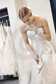 Beautiful confused woman in wedding dress holding footwear while looking down