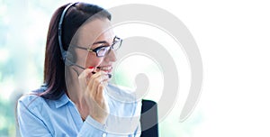 Beautiful consultant of call center in headphones.  Portrait of smiling female customer using headset at call center office