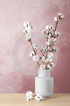 Beautiful cotton flowers in vase on wooden table against background