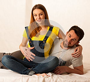 Beautiful coule - young man and pregnant woman resting on bed