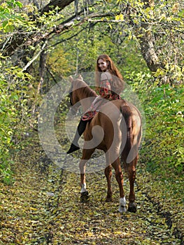 Beautiful country girl bareback ride her horse in autumn country road at sunset