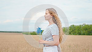 Beautiful country lady with a long curly hair walking through the wheat field and holding a colorful wind spinner in