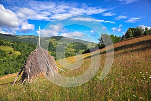 Beautiful countryside landscape with forested hills and haystacks on a grassy rural field in mountains