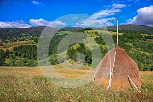 Beautiful countryside landscape with forested hills and haystacks on a grassy rural field in mountains