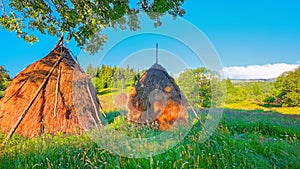 Beautiful countryside landscape with forested hills and haystacks on a grassy rural field in mountains