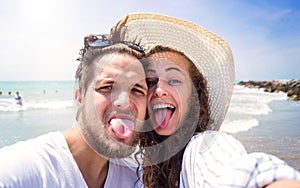 Beautiful couple on beach, laughing, taking selfie, sticking out