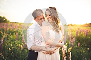 Beautiful couple, bride, groom kissing and hugging in the field sunset