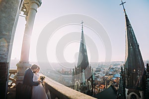 Beautiful couple, bride and groom posing on old balcony with column, cityscape background