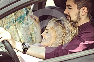 Beautiful couple in the car looks at the map. They are smiling at the wheel. The best travel route