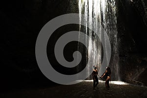 Beautiful couple in a cave with a waterfall. Athletic man and woman under the streams of a waterfall.