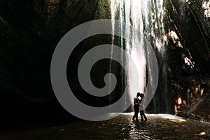 Beautiful couple in a cave with a waterfall. Athletic man and woman under the streams of a waterfall.