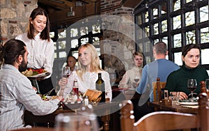 Beautiful couple eating out at a restaurant while young and obliging waitress is serving them dishes