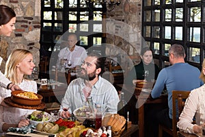 Beautiful couple eating out at a restaurant while young and obliging waitress is serving them dishes