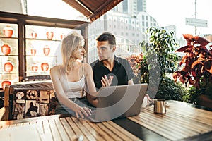 Beautiful couple girl sitting on terrace in restaurant with laptop on table, drinking coffee, and talking. Students sitting in