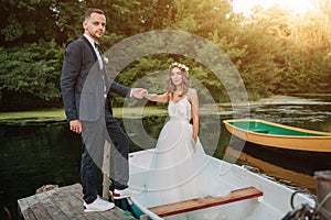 Beautiful couple groom and bride near river boat. Against the background of beautiful nature and sunset