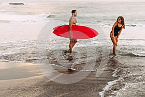 Beautiful couple have fun at the sea. Couple in love on the beach with a surfboard at sunset.