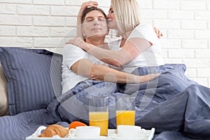 Beautiful couple having breakfast lying in bed at home. Handsome man and attractive woman are enjoying spending time