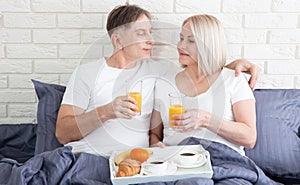 Beautiful couple having breakfast lying in bed at home. Handsome man and attractive woman are enjoying spending time