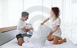 Beautiful couple having fun by fighting with a pillow on bed after waking up in bright bedroom
