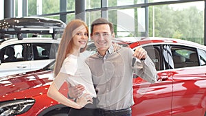 Beautiful couple is holding key of their new car, looking at camera and smiling