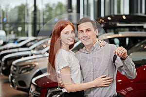 Beautiful couple is holding key of their new car, looking at camera and smiling