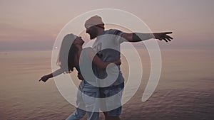 Beautiful couple hugs and kisses standing in the middle of the sea. Hipster guy and girl enjoy a vacation on sunset