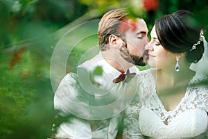 Beautiful couple kissing among spring foliage. Close up portrait of bride and groom at wedding day outdoor, lit by