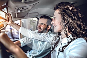 Beautiful couple is looking at rearview mirror and smiling while sitting in their new car