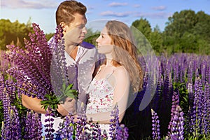 A beautiful couple in love on a blooming field with a bouquet of bright flowers