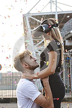 Beautiful couple in love having fun in a rain of colorful confetti with virtual reality glasses