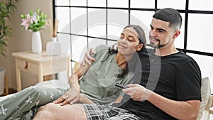 Beautiful couple lying in comfy bed, enjoying movie, joyfully smiling together in a relaxing bedroom atmosphere