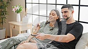 Beautiful couple lying in comfy bed, enjoying movie, joyfully smiling together in a relaxing bedroom atmosphere