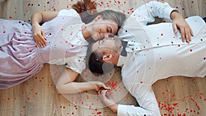 Beautiful couple lying on floor face to face while heart shape confetti falling down