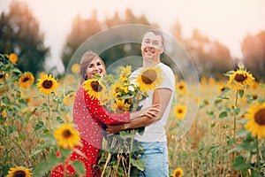 Beautiful couple man and woman in field sunflowers in red dress and hat, sunlight