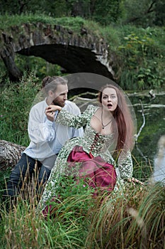 Beautiful couple man and woman in medieval costume style sitting on the tree