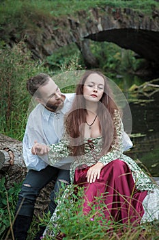 Beautiful couple man and woman in medieval costume style sitting on the tree