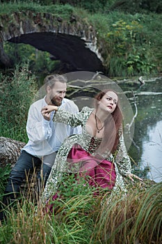 Beautiful couple man and woman in medieval costume style sitting on the tree