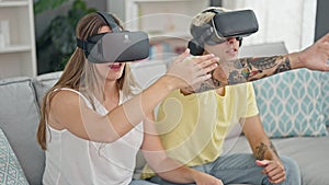 Beautiful couple playing video game using virtual reality glasses at home